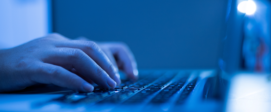 Image of user typing on laptop in blue lighting