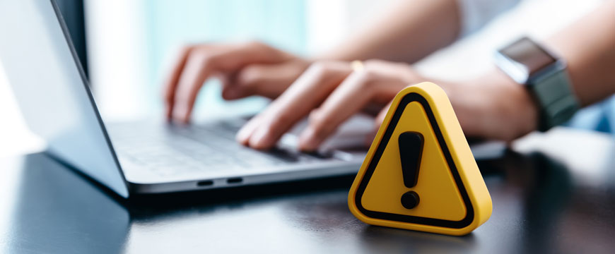 Person Typing on a Computer with an Alert Symbol