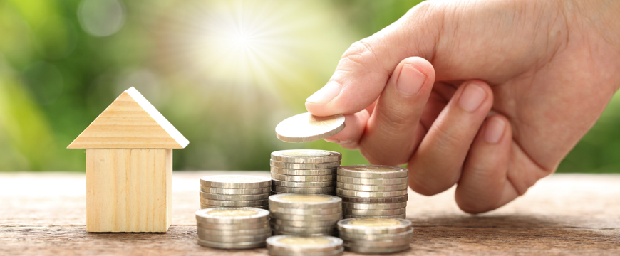 Person placing coins on a table next to a wooden house