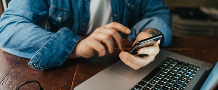 Person looking at their mobile device at a table with a laptop
