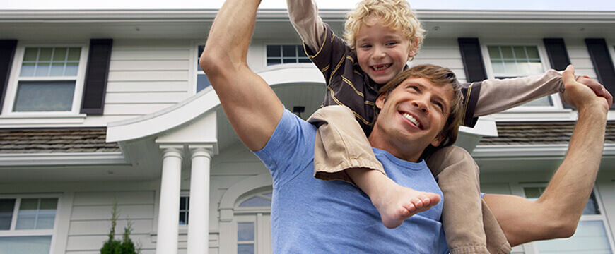 Mortgage Image - happy man with a child on his shoulders in front of a nice house